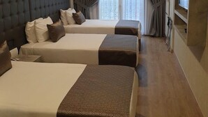 A hotel room with three beds, a large painting on the wall, a television, and a window with curtains. - Four Sides Sisli (Istanbul)