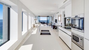 A modern kitchen with built-in appliances, a dining area with a view, and a spacious living room with a large window overlooking the ocean.