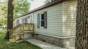 A single-story mobile home with a wooden deck and a small staircase leading to a front door. - Mooseyard Lodge (Shawano)