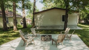 A patio area with four wooden chairs arranged around a fire pit, set against a house with a light-colored exterior. - Mooseyard Lodge (Shawano)