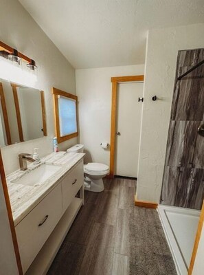 A bathroom with a marble sink, a toilet, and a shower with a wooden door. - Mooseyard Lodge (Shawano)