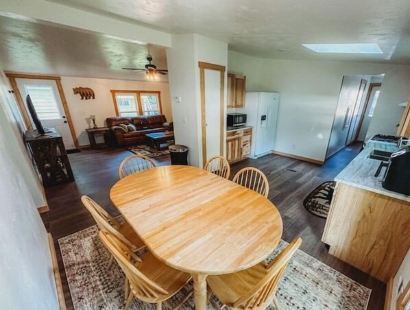 A dining area with a wooden table and chairs, a kitchen with modern appliances, and a living room with a sofa and a bear decoration. - Mooseyard Lodge (Shawano)