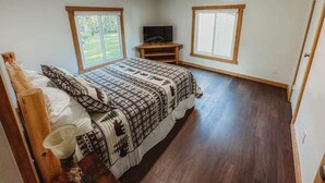 A bedroom with a bed, a TV on a wooden stand, and two windows with wooden frames. - Mooseyard Lodge (Shawano)