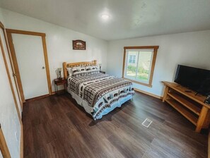 A bedroom with a bed, a nightstand, a TV stand, and a window. - Mooseyard Lodge (Shawano)
