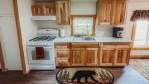 A kitchen with wooden cabinets, a gas stove, a sink, and a coffee maker. - Mooseyard Lodge (Shawano)