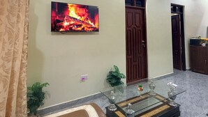 A living room with a flat-screen TV displaying a fire, a glass coffee table, leather sofas, and a wooden door.