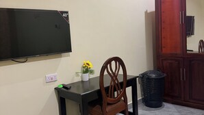 A room with a desk, chair, TV, cabinet, and trash can.