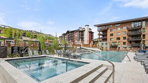 A hotel pool area with two swimming pools, lounge chairs, and a view of surrounding buildings.