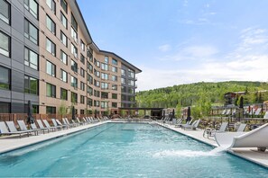Relax by the pool surrounded by lounge chairs and umbrellas in a scenic hillside setting.