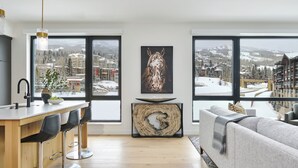 A modern living room with a large window, a dining area with bar stools, and a sofa.