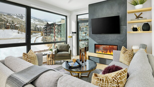 A modern living room with a fireplace, large windows, and a view of a snowy landscape.