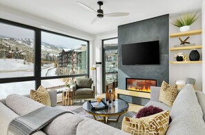 Relax in this cozy living room with a panoramic view of the surrounding mountains, featuring a comfortable sofa, coffee table, and flat-screen TV.