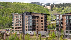 A modern multi-story building with a mix of glass and wood facade, surrounded by a forested hillside.