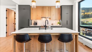A modern kitchen with a central island, bar stools, wooden cabinets, and pendant lighting.