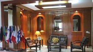 A lobby with wooden paneling, a seating area with leather chairs, a coffee table, and a display of flags. - Edificio Asuncion (Asunción)