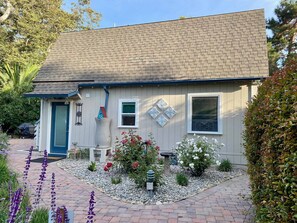 Guests enter through a charming front door with a blue frame, surrounded by lush gardens and a gravel pathway.