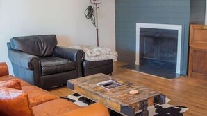 Un salon avec une cheminée, des canapés en cuir, une table basse et un ventilateur de plafond.