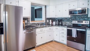 Une cuisine moderne avec des armoires blanches, des appareils en acier inoxydable, un pare-feu en carrelage et un plancher en bois.