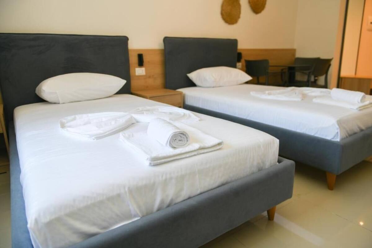 A hotel room with two beds, each with a headboard, a nightstand, and a chair.