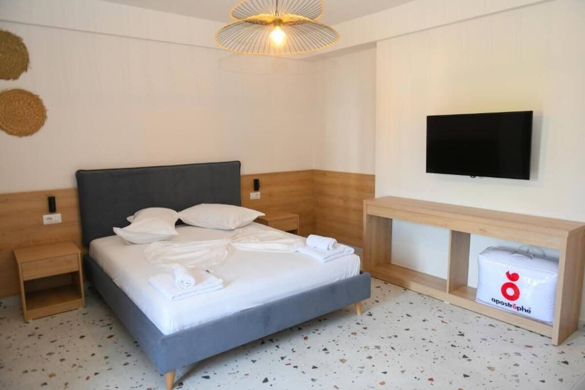 A hotel room with a bed, a TV mounted on the wall, a wooden nightstand, and a small wooden table with a towel on it.