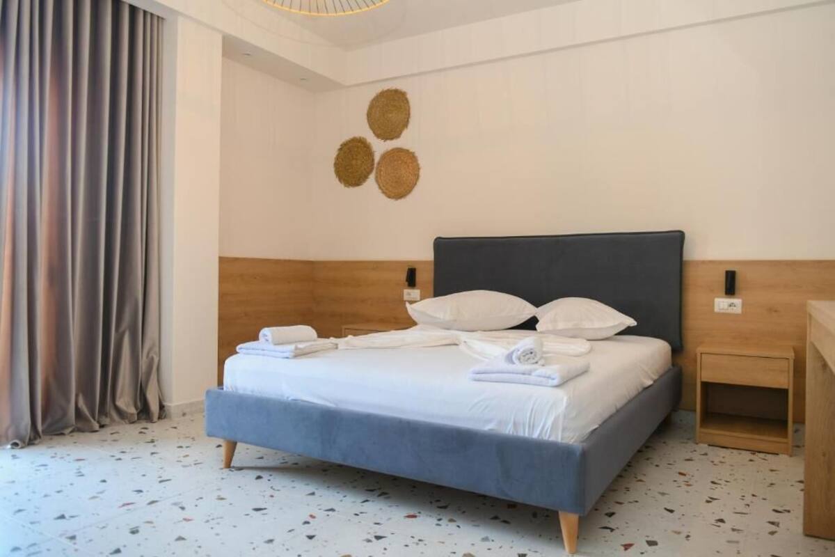 A neatly made bed with white linens and pillows, a wooden headboard, and a small wooden nightstand with a lamp.