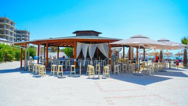 Een buitenmeubilairgedeelte met tafels en stoelen onder een overdekte pergola.