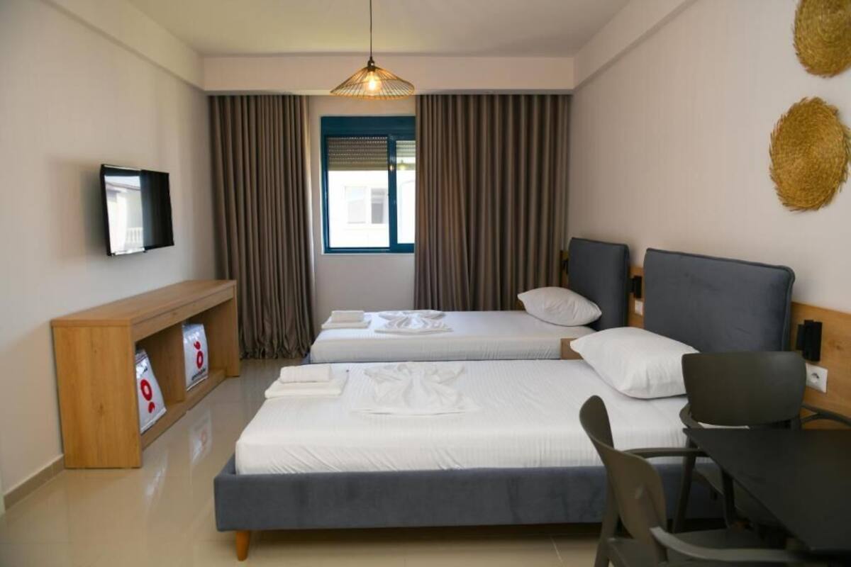 A hotel room with two beds, a desk, a TV, and a window with curtains.