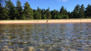 Ein klarer See mit Sandstrand und dichtem Wald im Hintergrund.