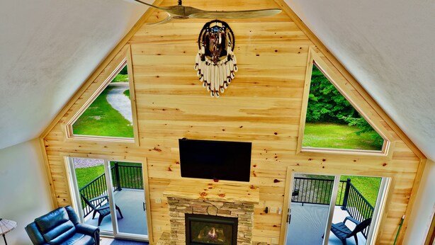 Ein gemütliches Blockhäuschen-Interieur mit Kamin aus Stein, Holzwänden und großen Fenstern mit Blick ins Freie.