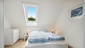 A bedroom with a sloped ceiling, a skylight, a bed with a checkered blanket, bedside lamps, a small white nightstand, and a framed picture on the wall. - Awesome home in Bække with kitchen (Bække)