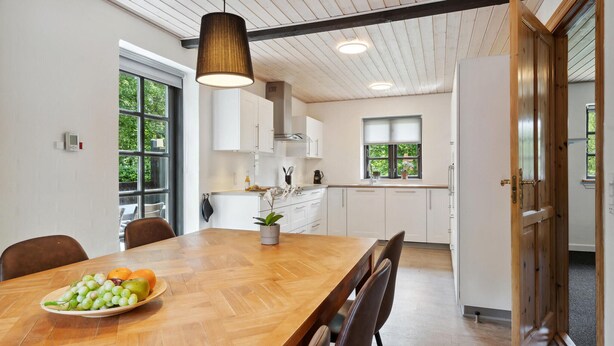 A modern kitchen with white cabinets, a wooden dining table, and a hanging light fixture. - Awesome home in Bække with kitchen (Bække)