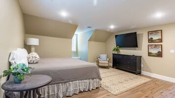A bedroom with a large bed, a dresser, a TV mounted on the wall, and a small table with a plant.