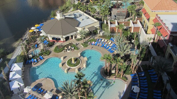 An aerial view of a resort with a central swimming pool, sun loungers, and palm trees.