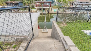 A concrete staircase leading to a dock area with a small boat, surrounded by a chain-link fence and greenery.