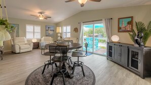 A spacious living room with a round dining table, two ceiling fans, a sofa, and a view of the outdoors.