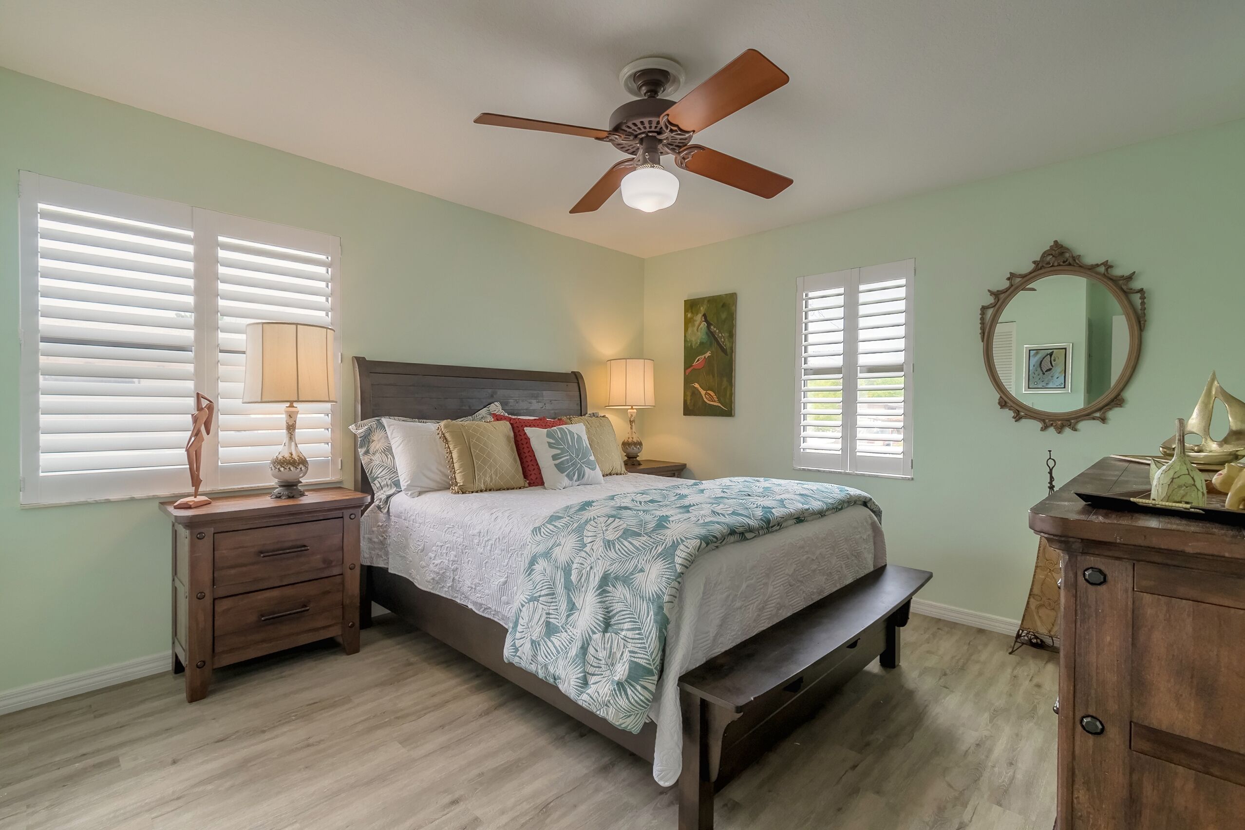 A bedroom with a bed, nightstands, a dresser, a ceiling fan, and a window with blinds.