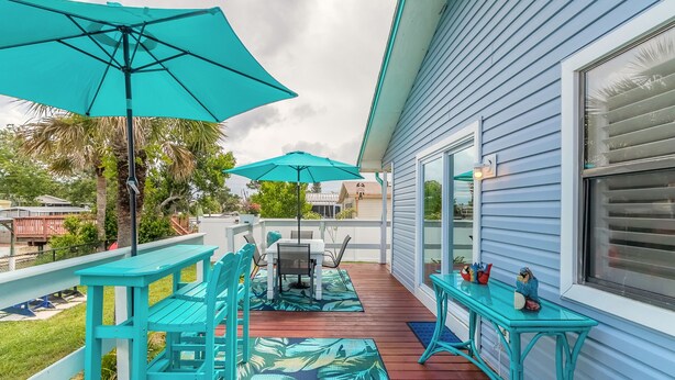 A covered patio with turquoise furniture, a table, and chairs, and a small table with decorative items.