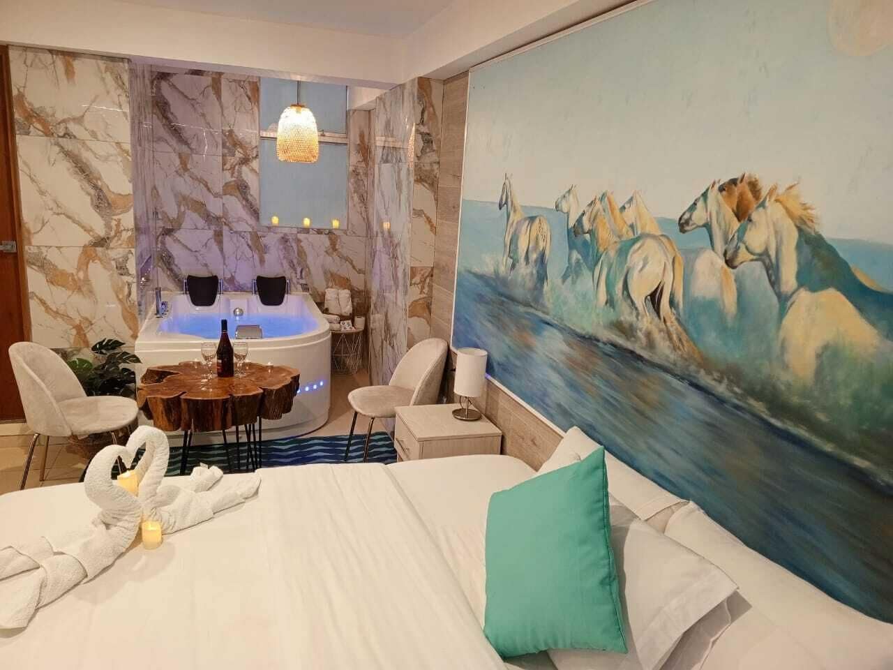 A hotel room with a large bed, a painting of horses, a massage chair, a massage table, and a jacuzzi.