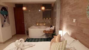 A modern bedroom with a large bed, a bathtub, and a small table with towels. - Hotel Jimenez Inn (Cusco)