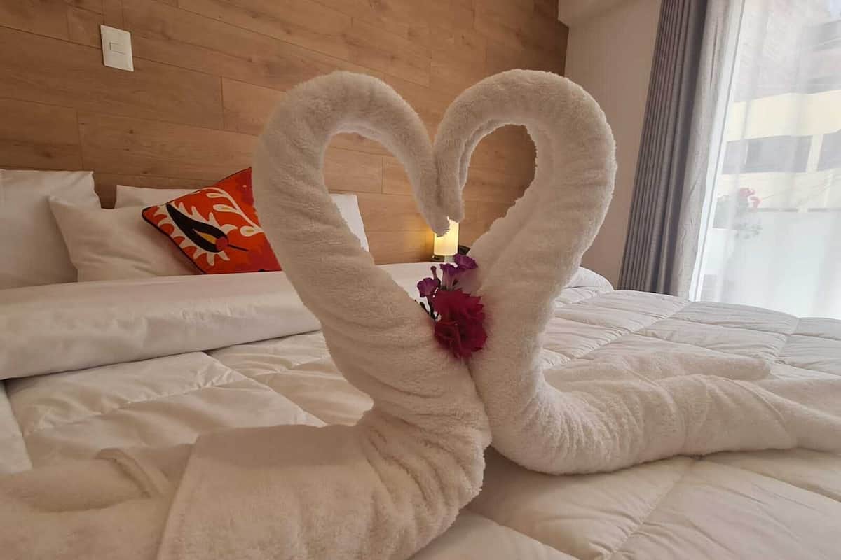 A bed with a heart-shaped towel arrangement and a small flower.