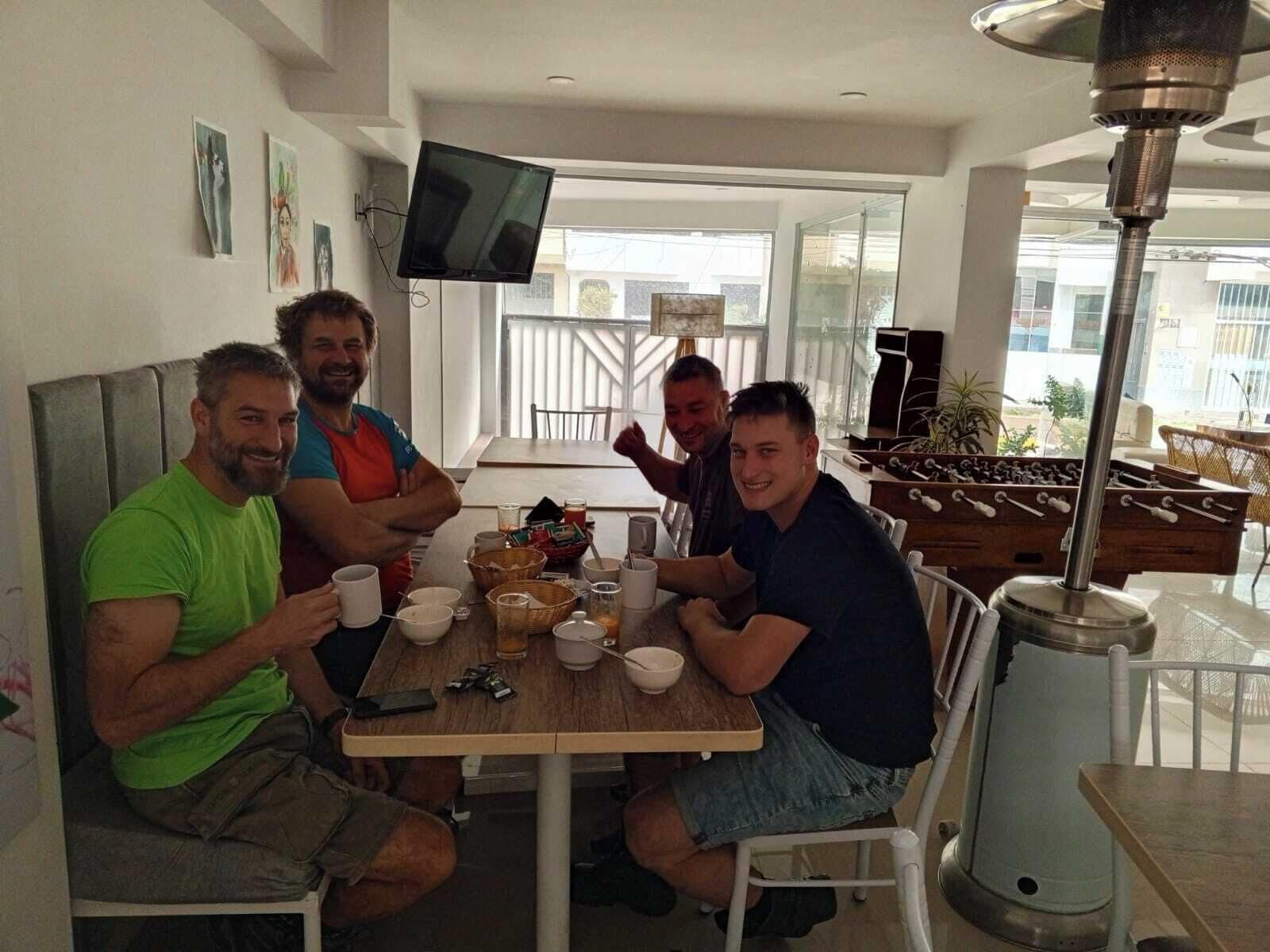 A dining area with a table set for four, a television mounted on the wall, and a foosball table in the background.