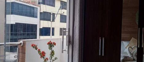 A balcony with a potted plant, a view of buildings, and a dark wooden wardrobe.
