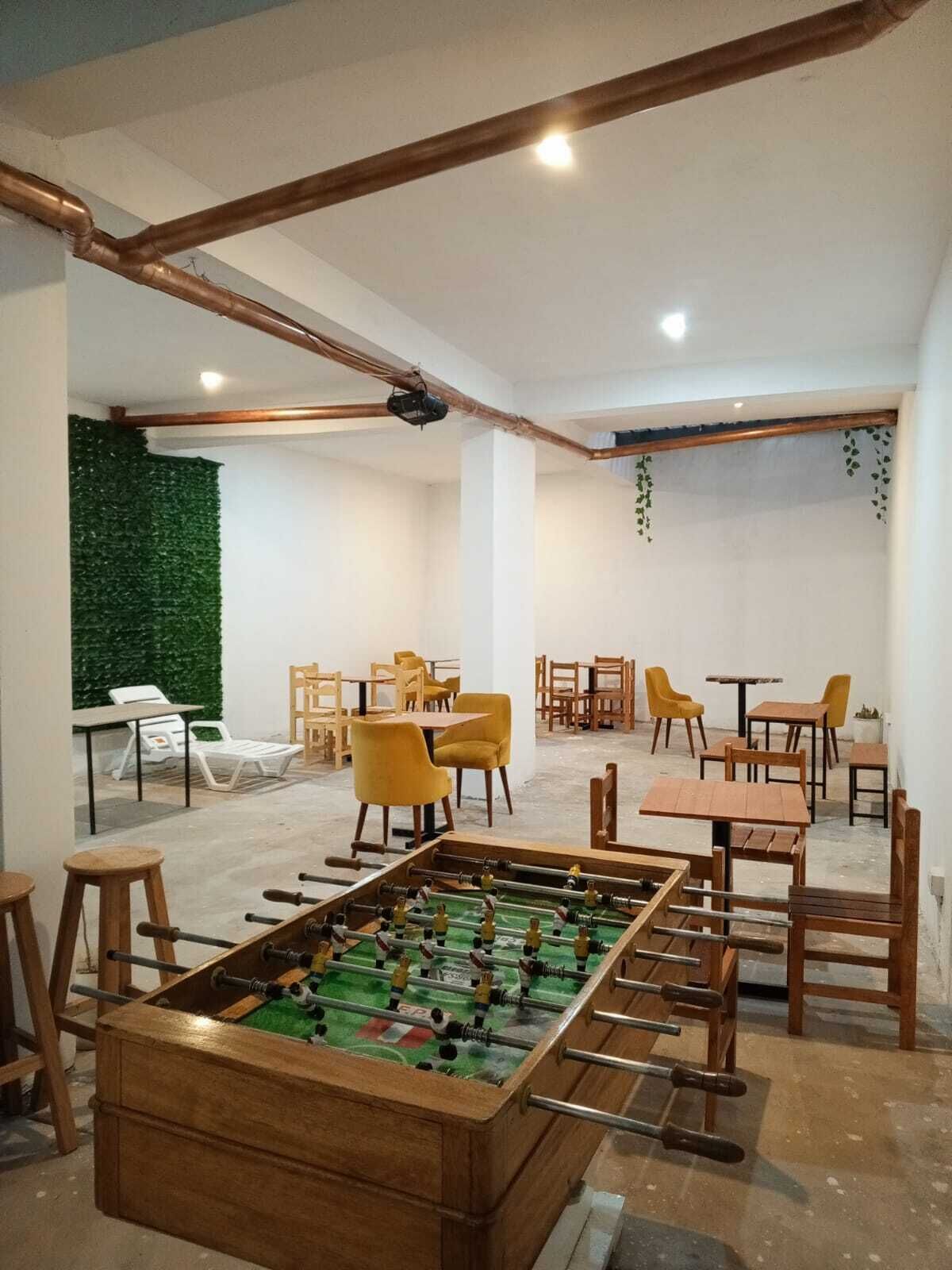 Una habitación con mesa de futbolín, sillas de madera y mesas dispuestas para comer.