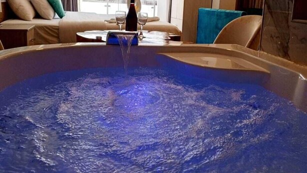 A modern hotel room with a large bathtub, a sofa, and a view of the cityscape. - Hotel Jimenez Inn (Cusco)