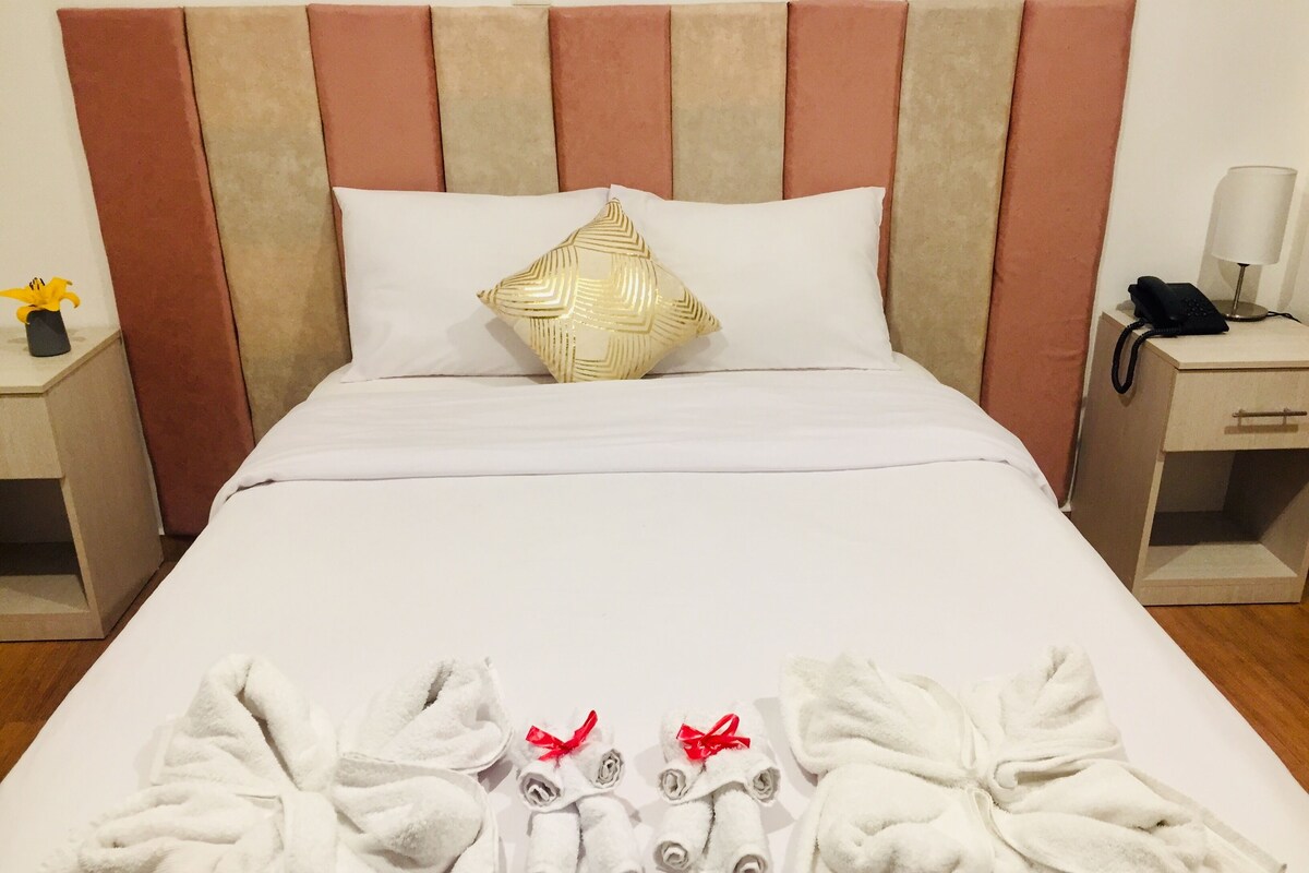 A neatly made bed with a striped headboard, a decorative pillow, and a set of towels arranged on the bed.