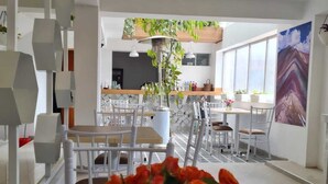 A modern dining area with white chairs and a wooden table, a hanging plant, and a large window with a mountain view. - Hotel Jimenez Inn (Cusco)