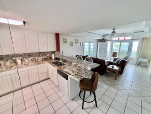A spacious kitchen with white cabinets, a granite countertop, and a dining area with a brown sofa and chairs. - Ship-Watch Dunes ~ Oceanfront ~ Dolphins! Pools! (Tybee Island)