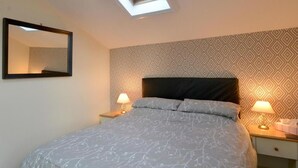 Un dormitorio con cama, dos mesitas de noche con lámparas, un espejo y papel tapiz estampado.