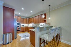 A modern kitchen with wooden cabinets, stainless steel appliances, a granite countertop, and a bar area with patterned stools.