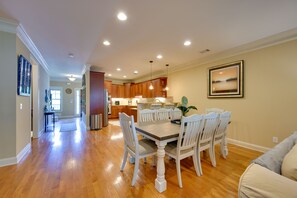 A spacious dining area with a wooden table and white chairs, a kitchen in the background, and a framed picture on the wall.
